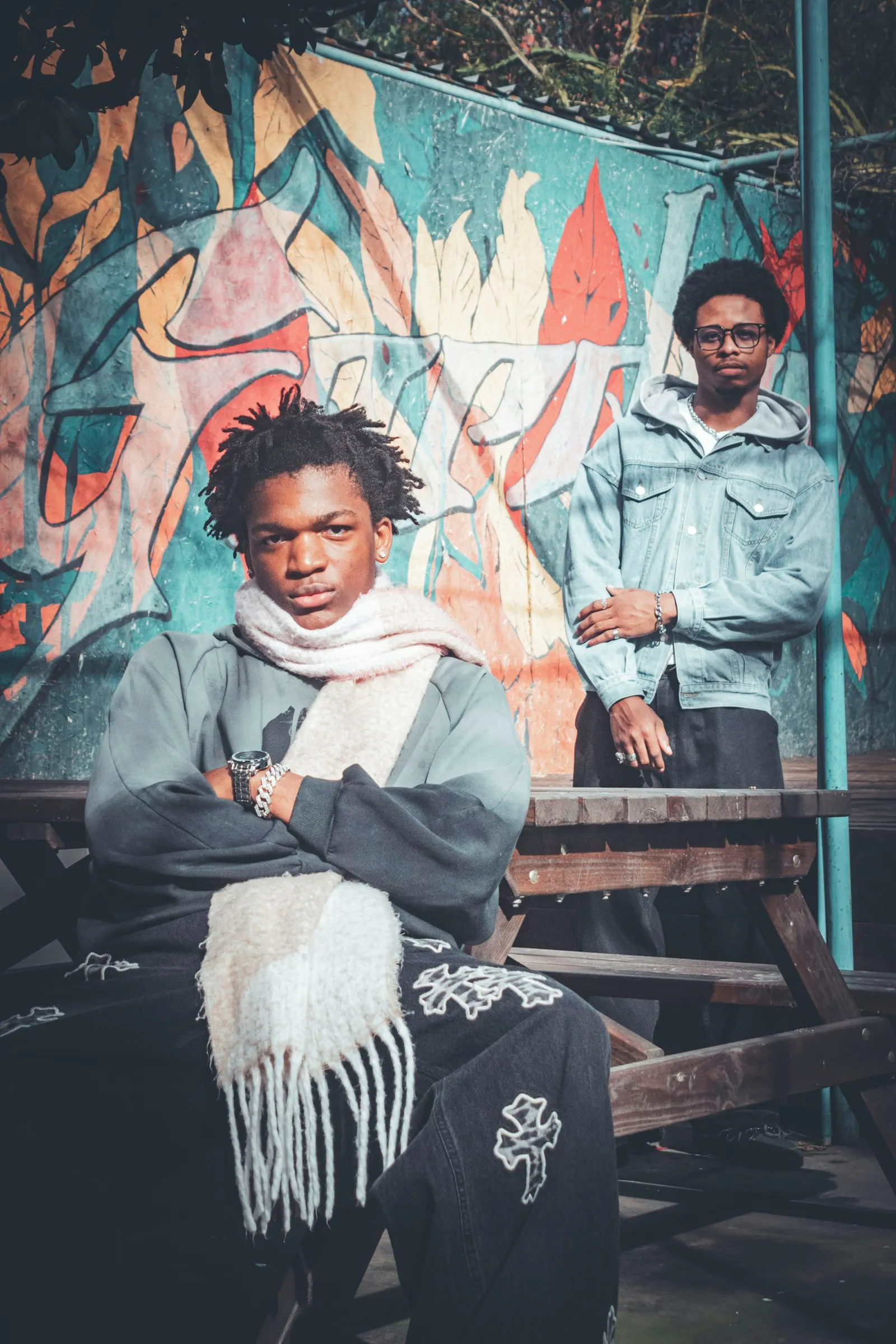 Two young men sitting on a bench in front of a painted mural