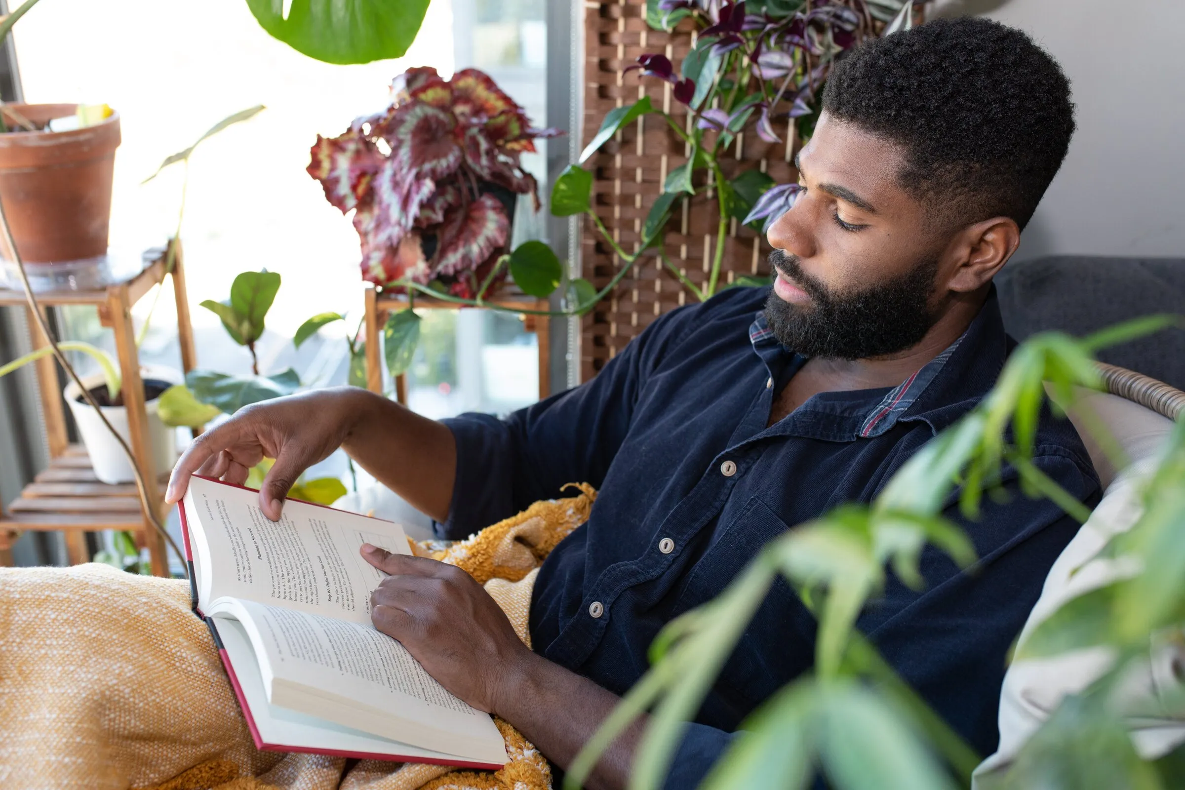 A young man reading at home, surrounded by plants