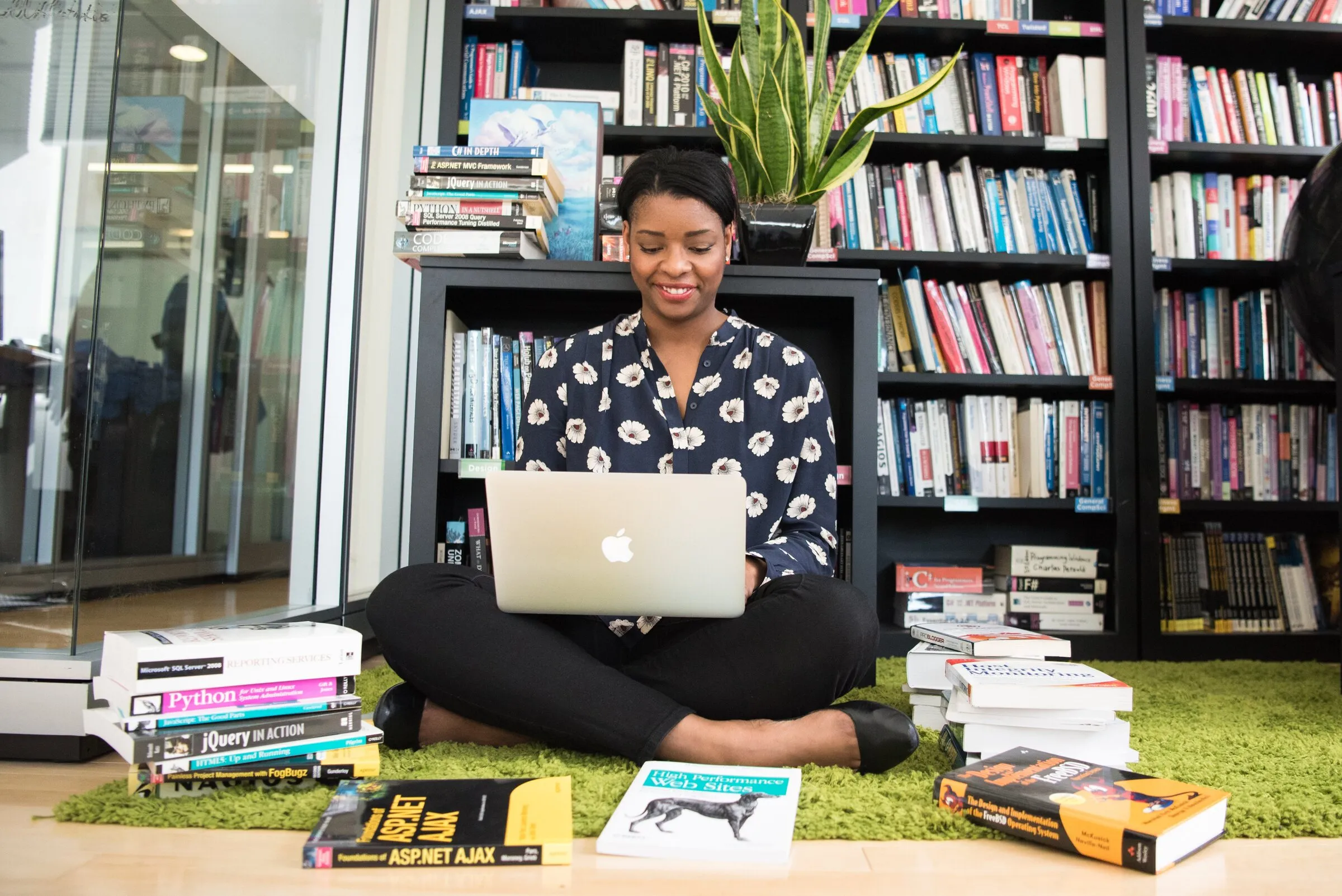 A young woman working on a laptop surrounded by programming books