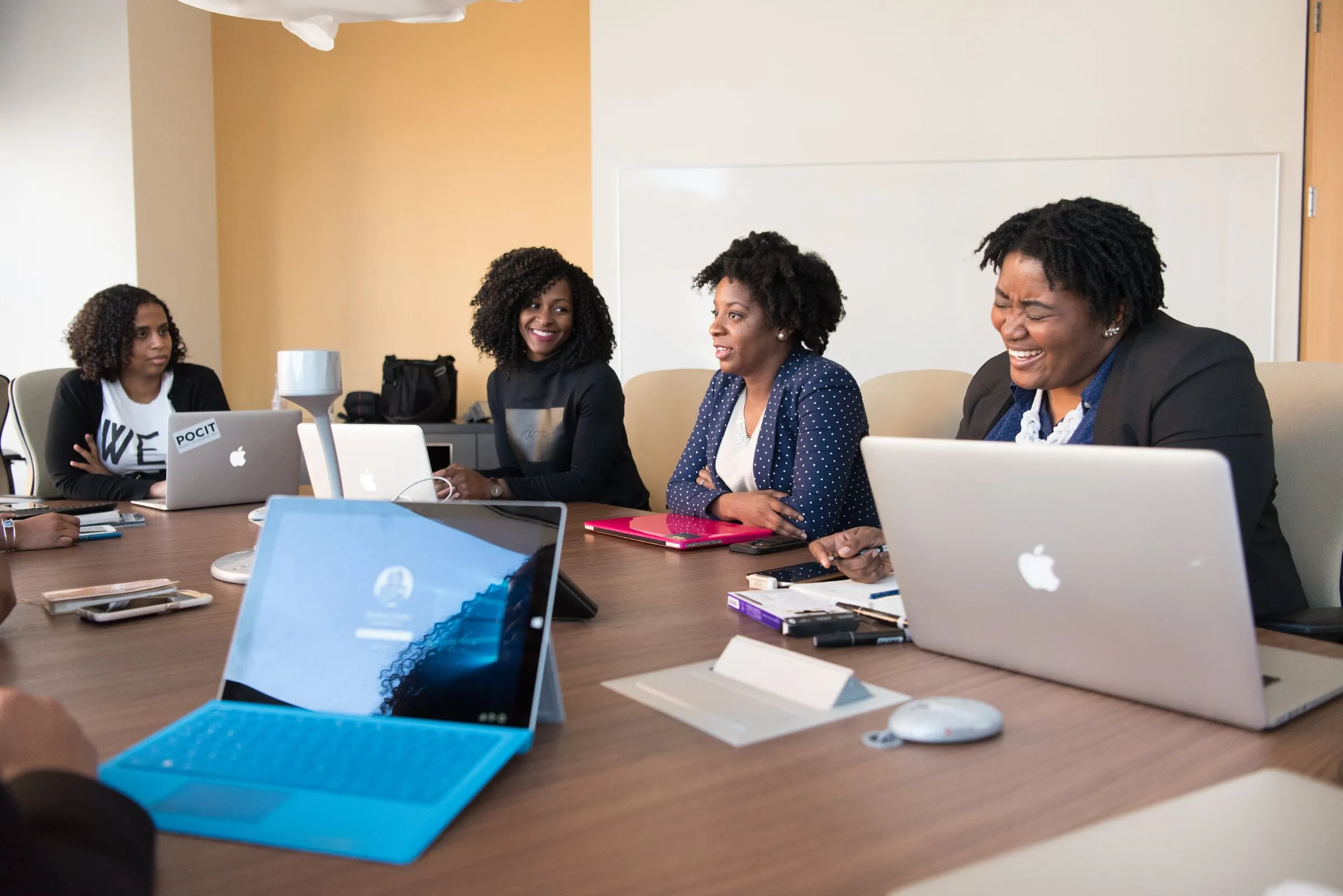 A group around a boardroom table with laptops open, mid meeting