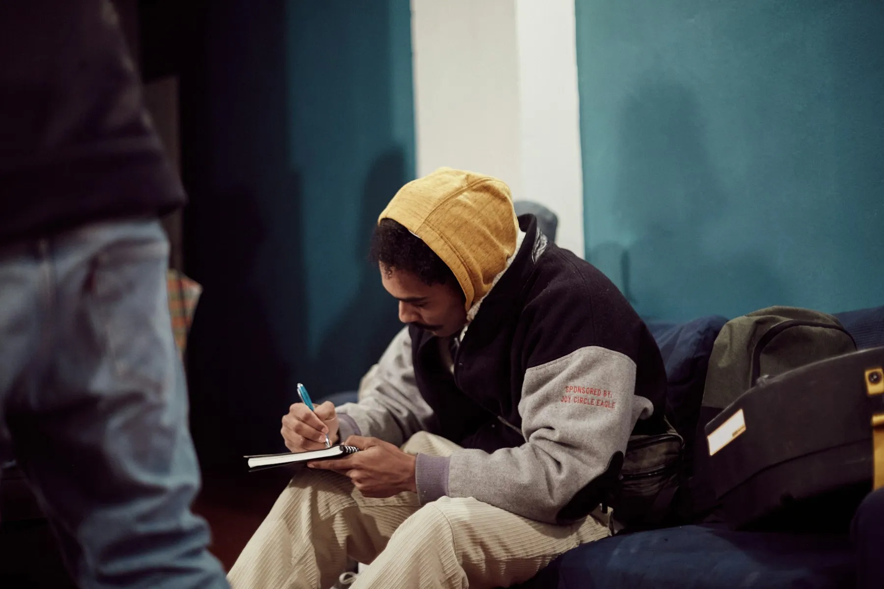 A young man sitting on a stoop, writing in a notebook
