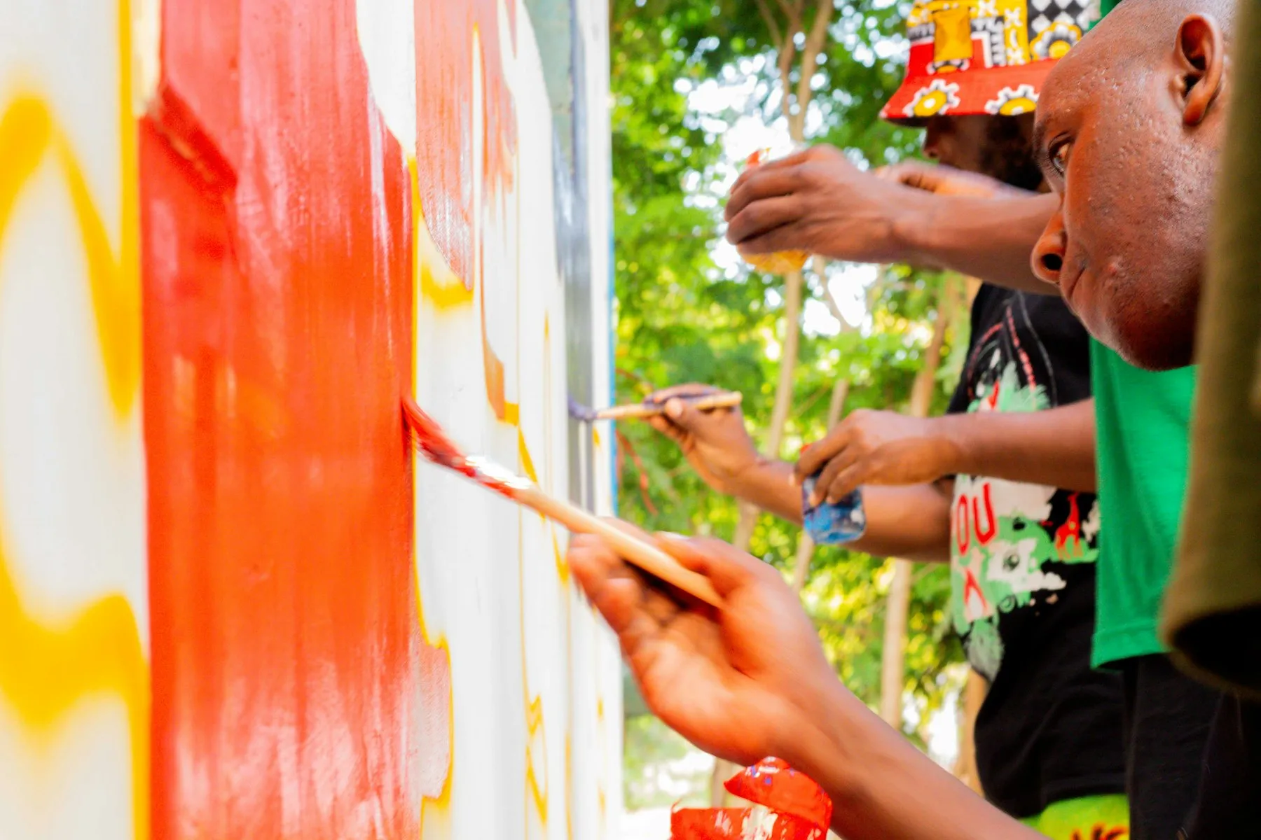 Hands painting a mural in red and yellow on a wall
