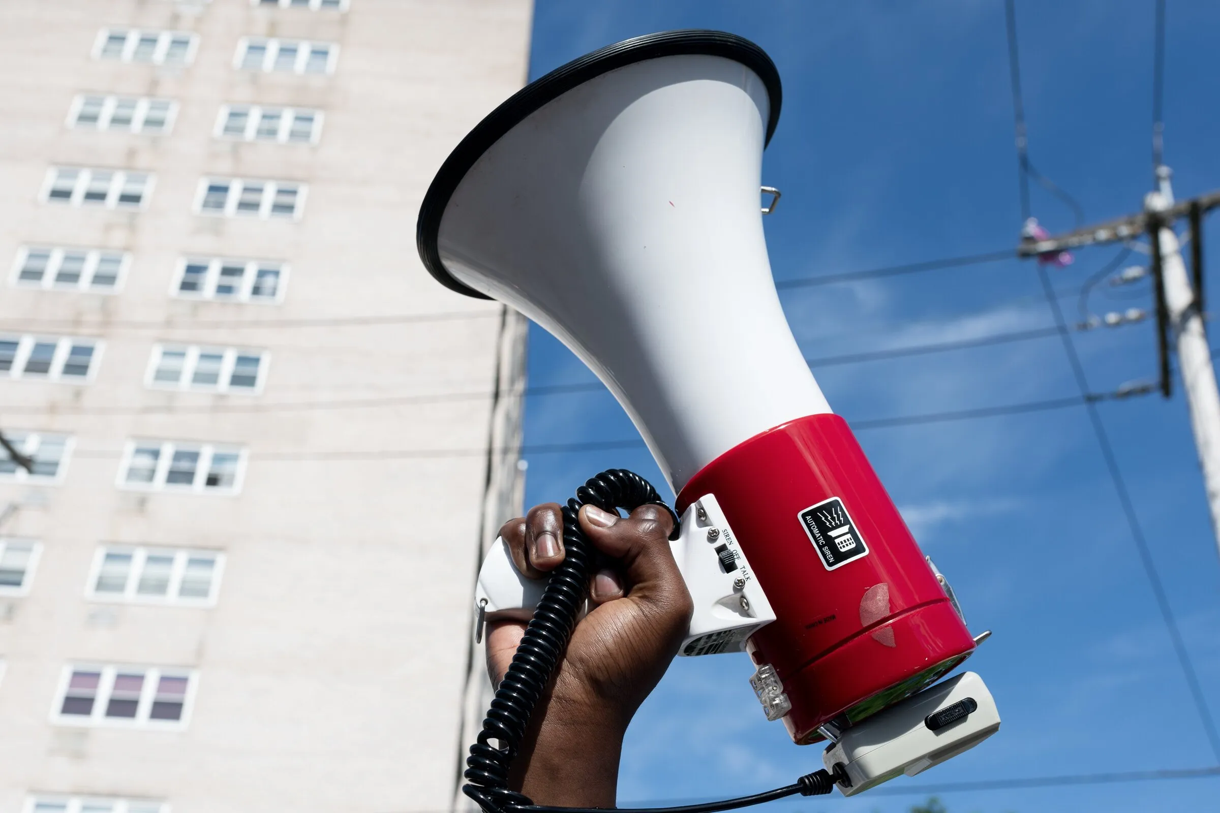 A hand holding a megaphone raised in front of an apartment block