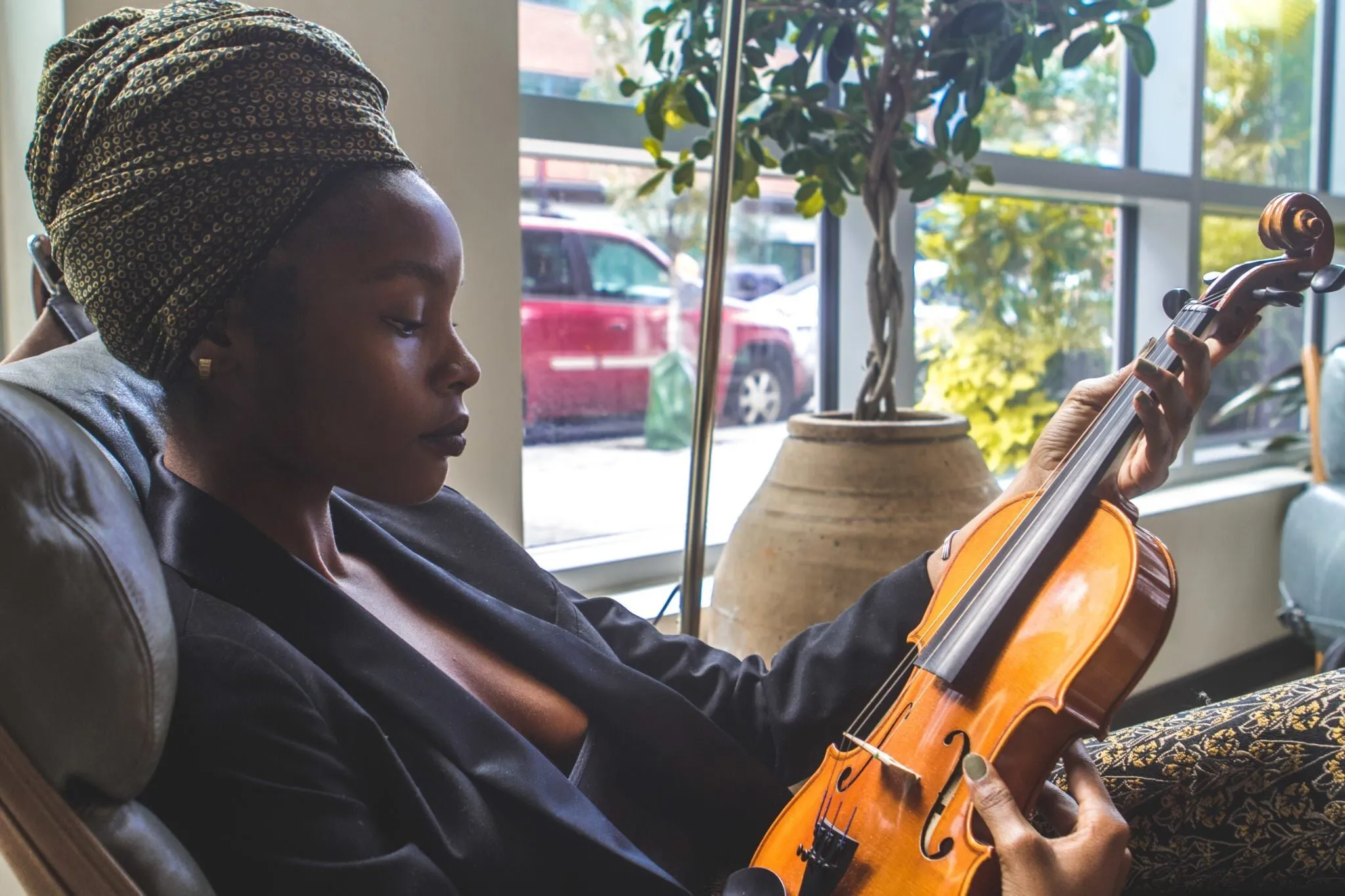 A young woman in a headwrap tuning a violin by a window